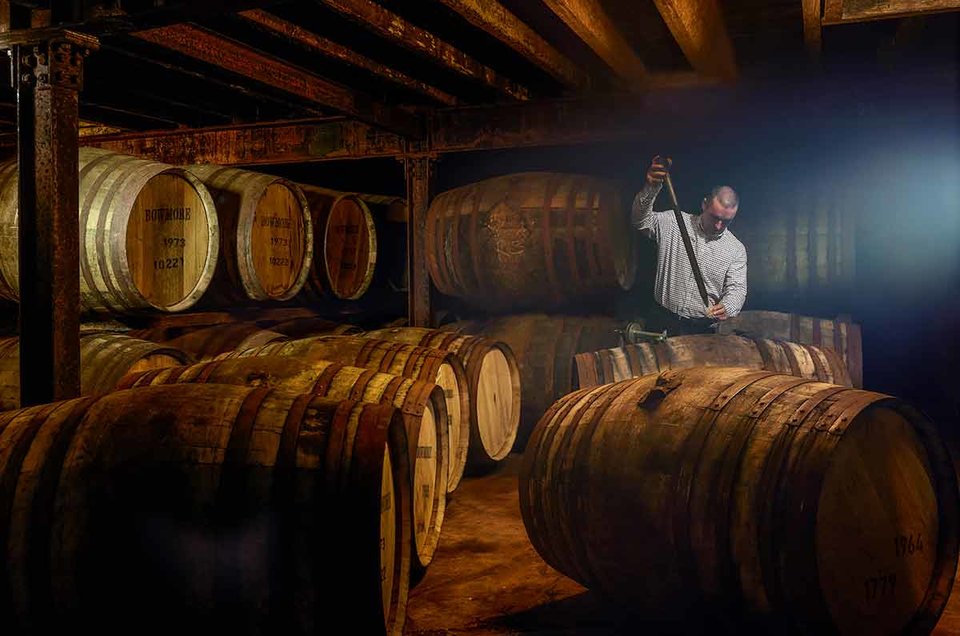 A man sampling whisky from a cask using a copper valinch