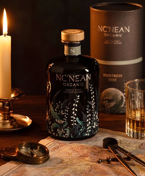 A bottle of Nc'nean Huntress whisky next to a candle, map of Scotland and compass.