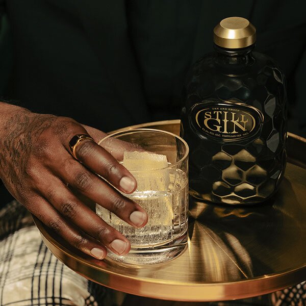 A hand holding a glass next to a bottle of Still G.I.N