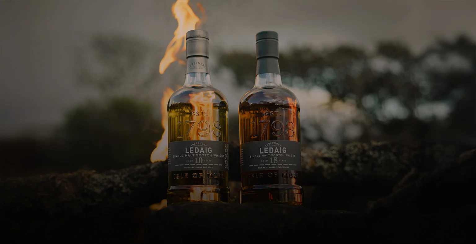 A bottle of Leldaig 10 year old and Ledaig 18 year old inf ront of a fire.