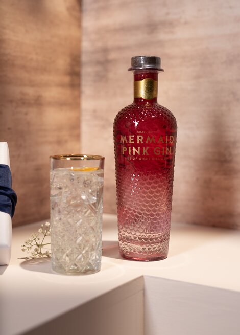 A bottle of Mermaid Pink Gin against a pink and beige background. 