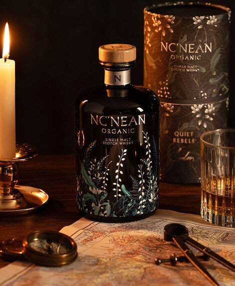 A bottle of Nc'nean Quiet Rebels whisky next to a candle, map of Scotland and compass.