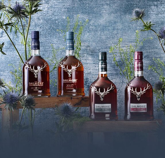 Four bottles of Dalmore whisky surrounded by thistles on a blue background.