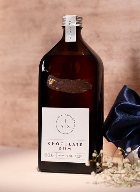 A bottle of Project 173 Chocolate Rum against a pink and beige background. 