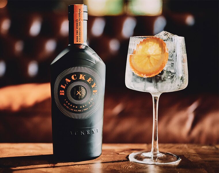 A bottle of Blackeye Gin with a perfect serve Gin & Tonic, garnished with an orange wheel.