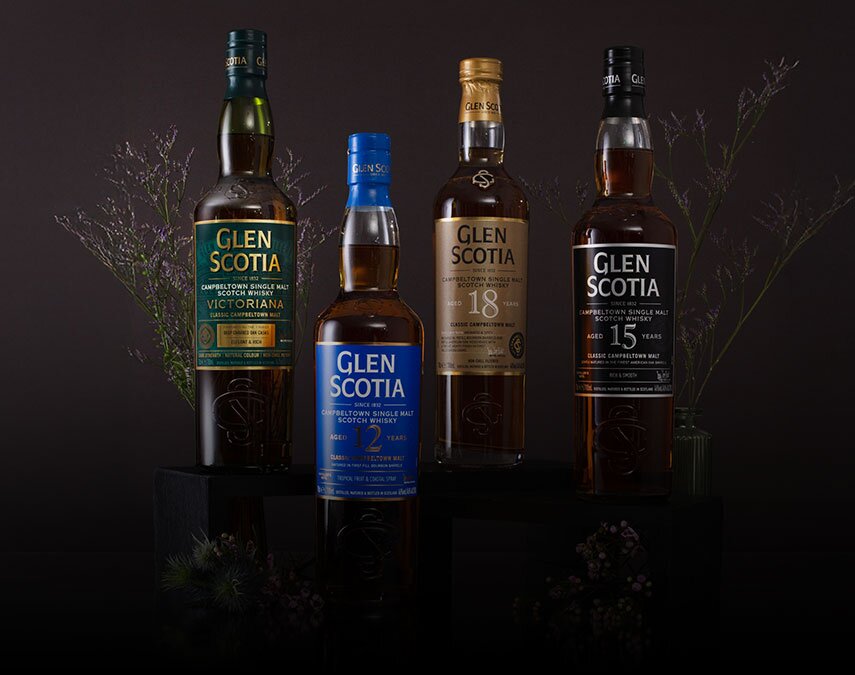 Four bottles of Glen Scotia whisky surrounded by thistles on a brown background.