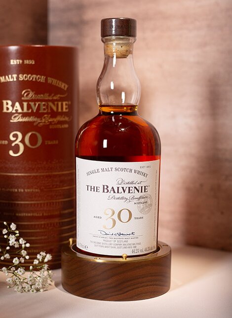 A bottle of Balvenie 30 year old whisky against a pink and beige background. 