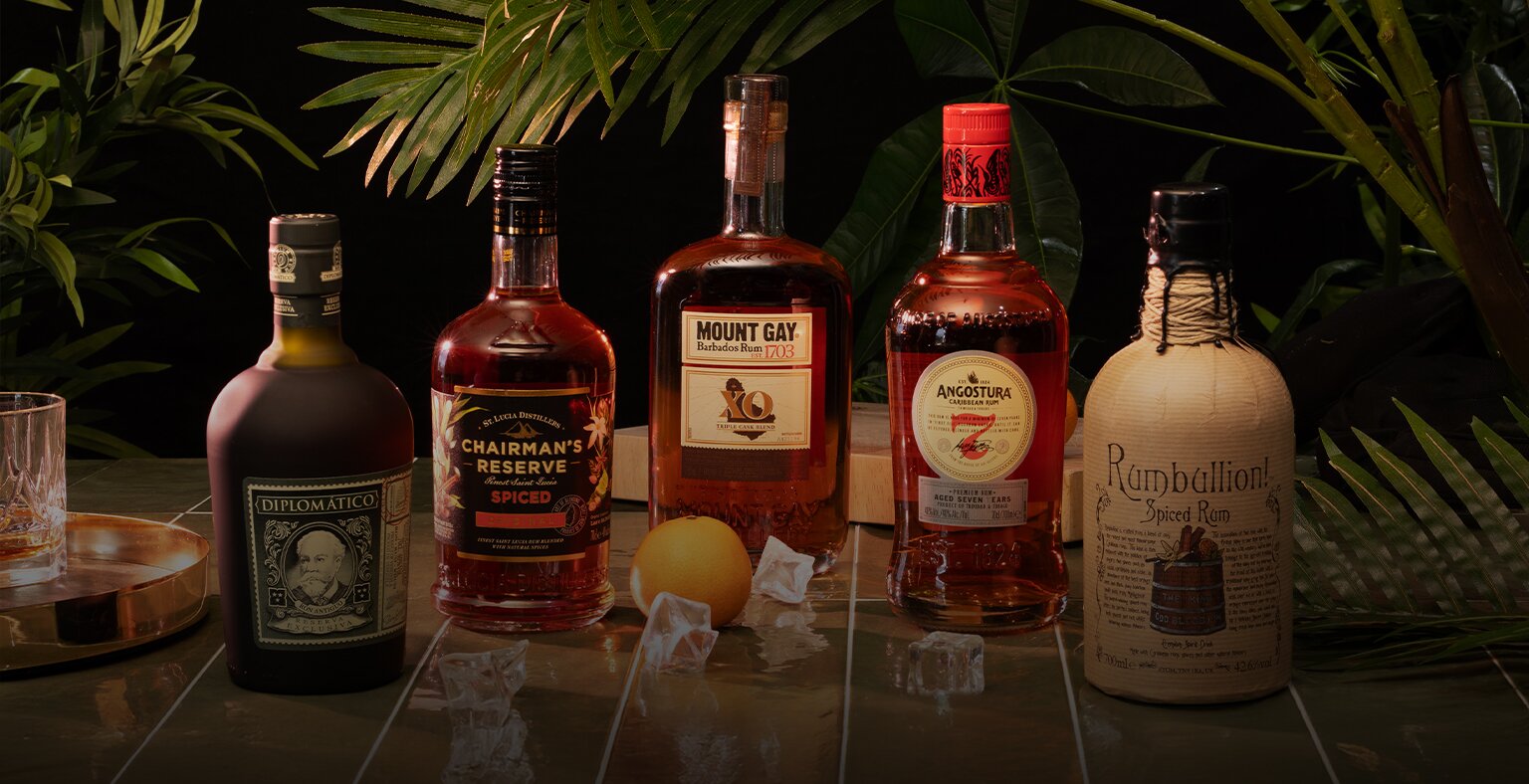 Five bottles of rum with tropical plants in the background, and a glass of rum to the left.