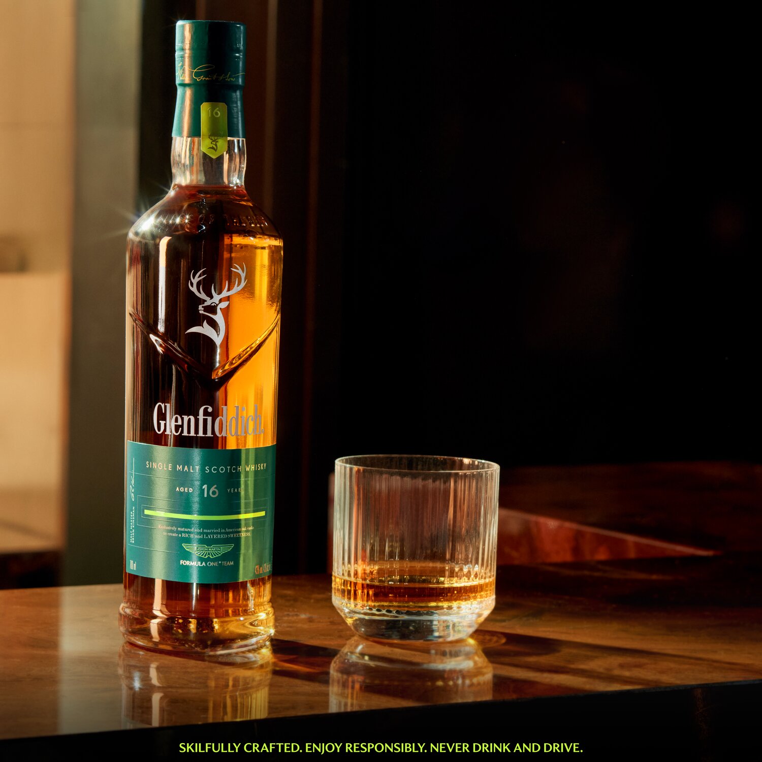 A bottle of Glenfiddich 16 Year Old x Aston Martin F1 next to a glass of whisky.