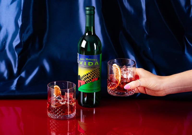 A bottle of Del Maguey Mezcal Vida in two glasses with ice and dried fruit.