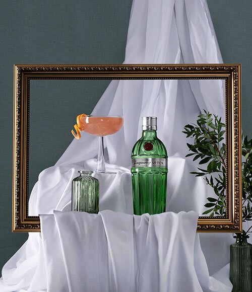 A bottle of Tanqueray No. 10 next to a Tiny 10 cocktail behind a gold picture frame.