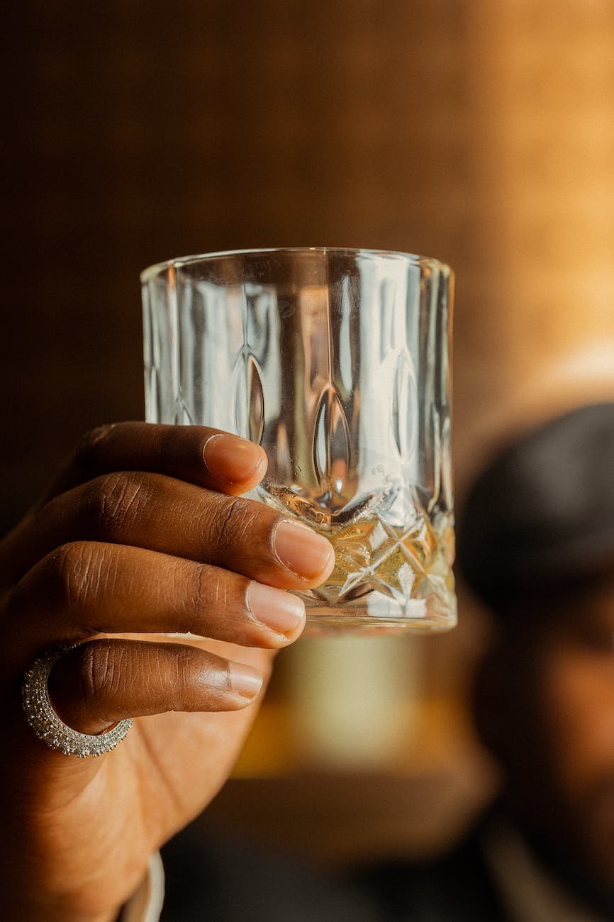 A person wearing a ring and holding a crystal tumbler of a clear alco