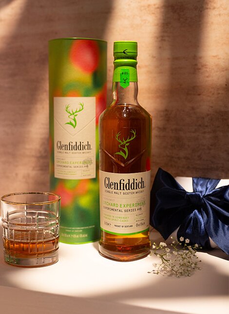 A bottle of Glenfiddich Orchard whisky against a pink and beige background. 