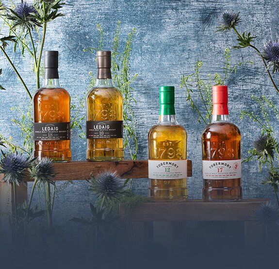 Four bottles of Tobermory and Ledaig whisky surrounded by thistles on a blue background.