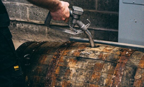A petrol pump nozzle filling up a whisky barrel. 