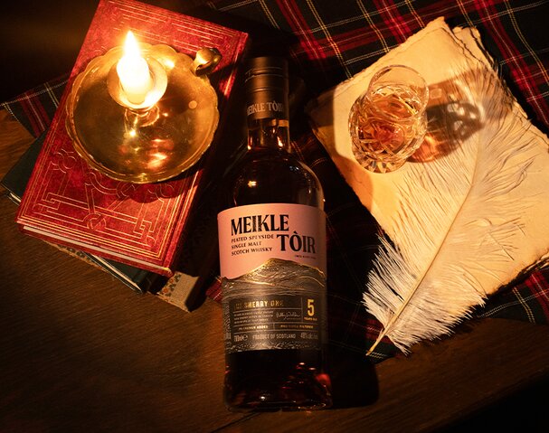 A bottle of Meikle Tòir The Sherry One whisky sitting on a pile of books in a library.