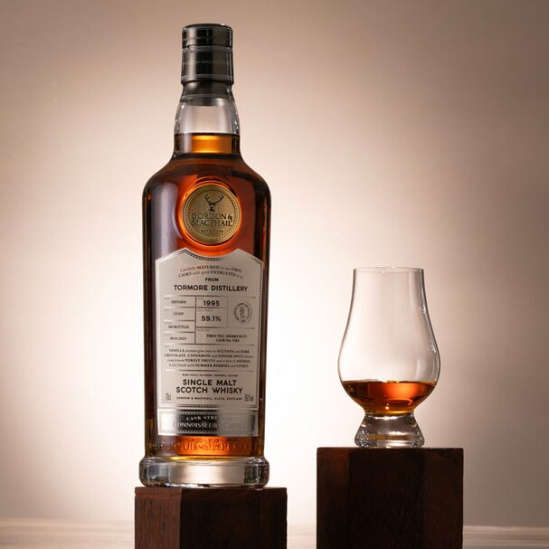 A bottle of Tomore 27 Year Old on a plinth, next to a Glencairn glass. 