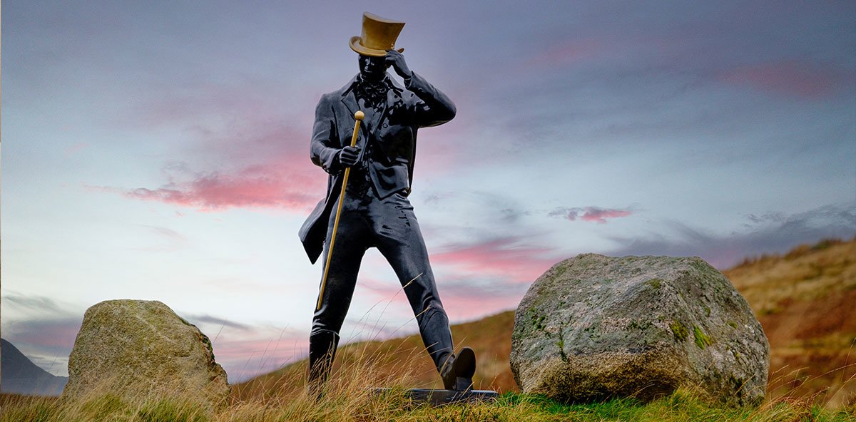 Johnnie Walker logo statue, with a golden top hat and walking cane, walking through a  field with boulders.