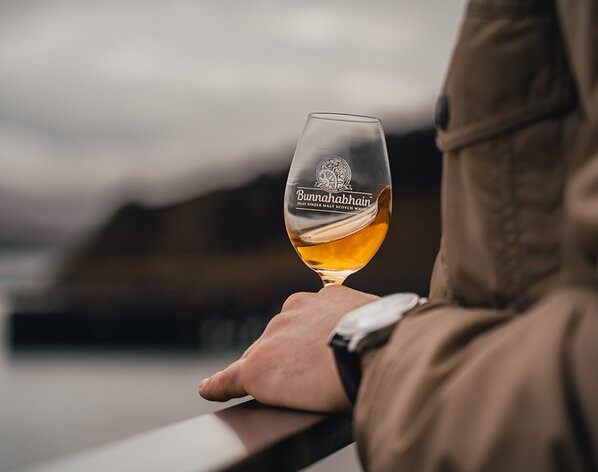 A glass of whisky in a Bunnahabhain branded glass being held