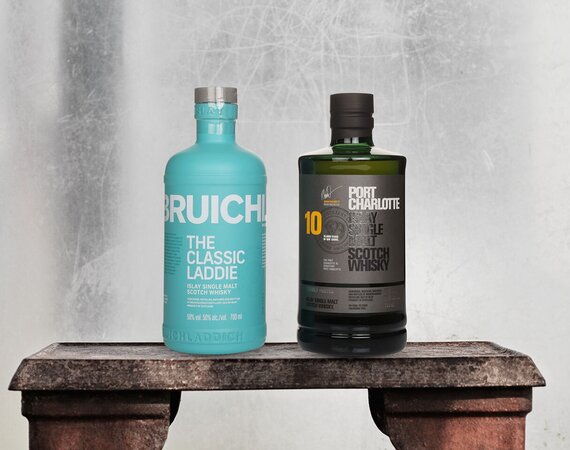 A bottle of Bruichladdich The Classic Laddie and Port Charlotte 10 on a stone bench.