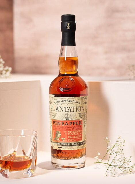 A bottle of Plantation Pineapple Rum against a pink and beige background.  