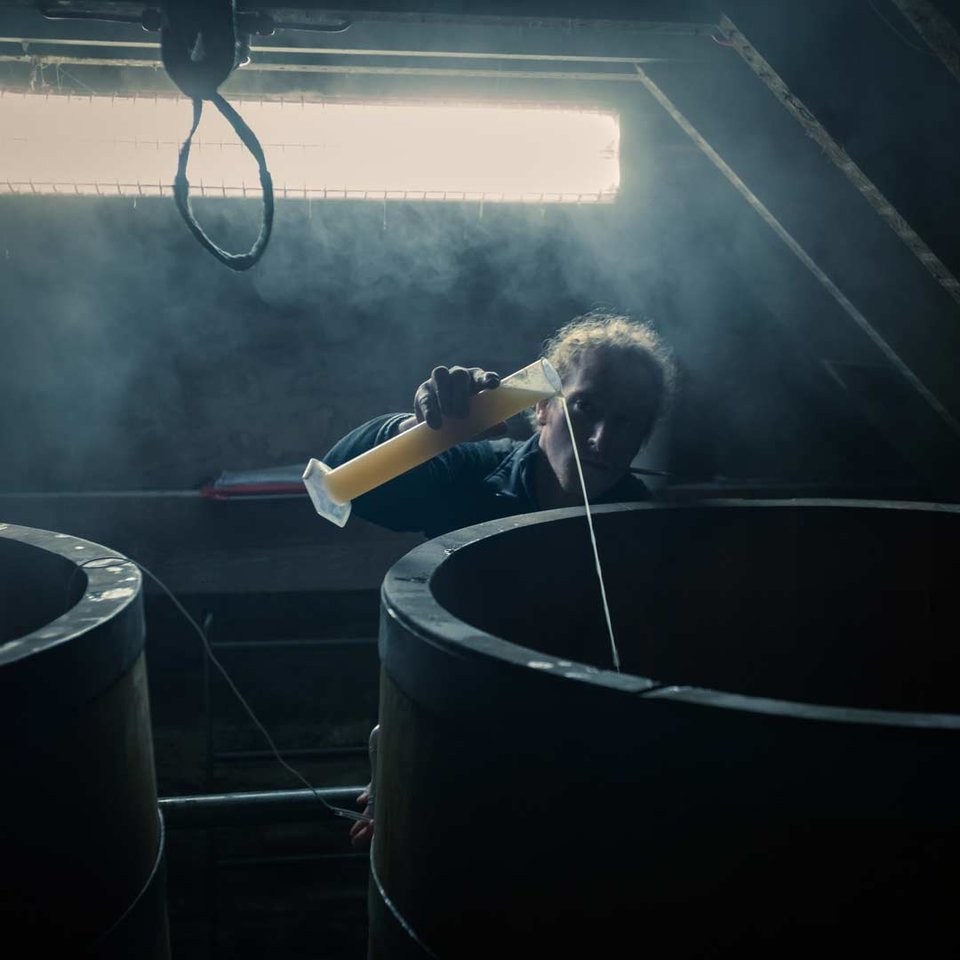 Liquid brewers yeast being poured from a measuring cylinder into an open top oak washback