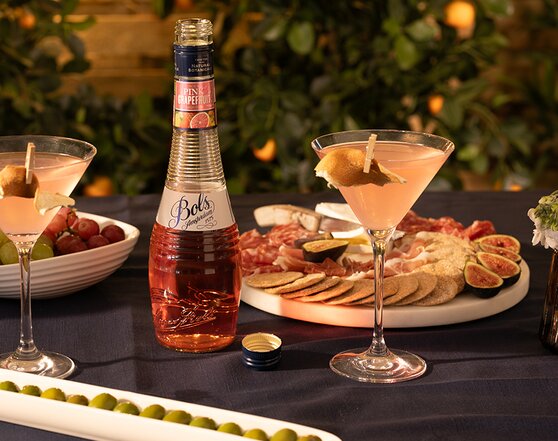 A Bols Pink Grapefruit Verano cocktail with a bottle of Bols Pink Grapefruit Liqueur next to it.
