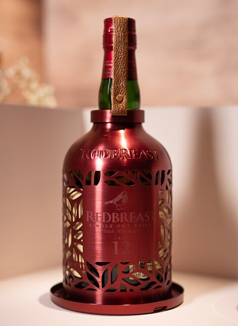 A bottle of Redbreast whiskey with a bird feeder against a pink and beige background. 