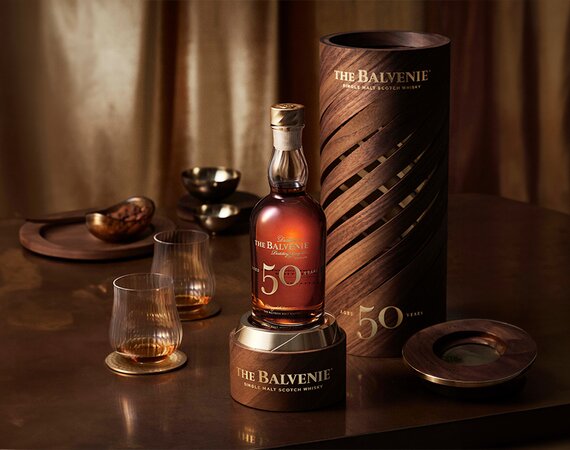 A bottle of The Balvenie 50 Year Old next to its presentation box and a glass of whisky. 