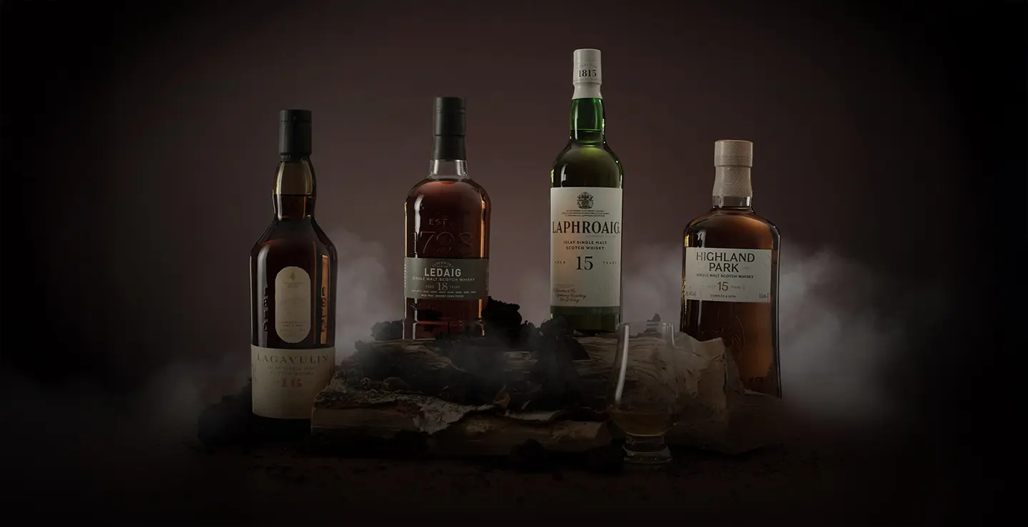 Bottles of peated whisky against a grey backround surrouned by chunks of peat. 