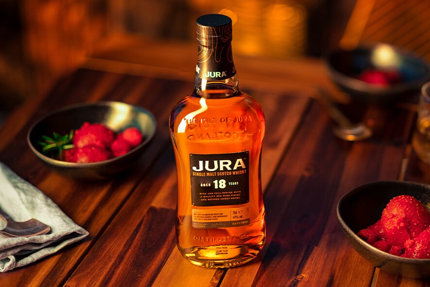 A bottle of Jura 18 year old on a wooden table next to bowls of sorbet. 