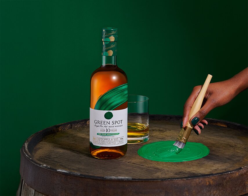 A bottle of Green Spot 10 Year Old 100 Year Anniversary bottle and a woman painting a spot of green paint.