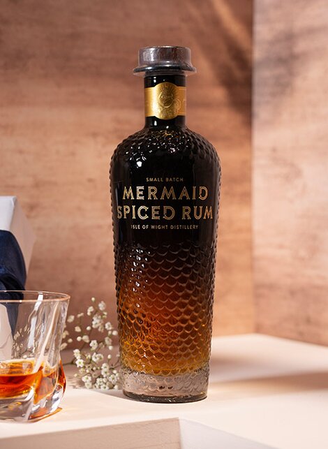 A bottle of Mermaid Spiced Rum against a pink and beige background. 