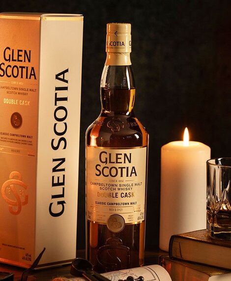 A bottle of Glen Scotia Double Cask whisky next to a stack of books and a candle. 