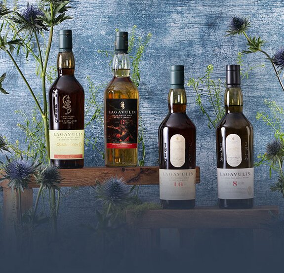 Four bottles of Lagavulin whisky surrounded by thistles on a blue background.