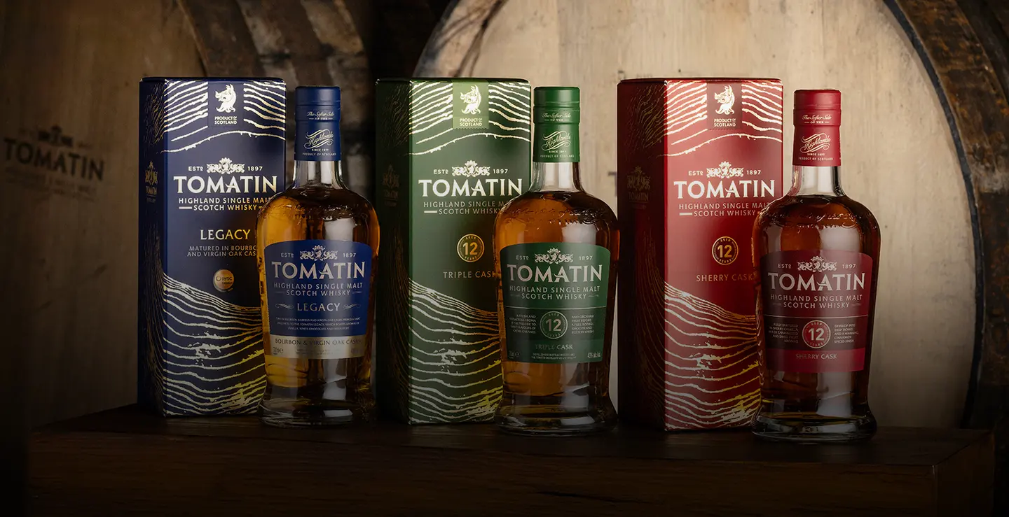 Three bottles of Tomatin whisky against the distillery building.