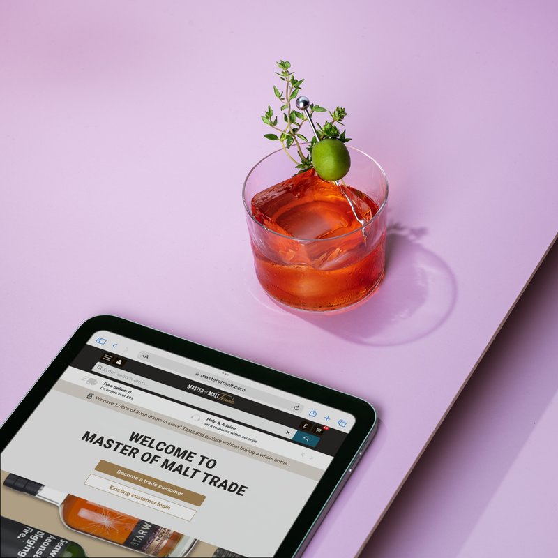 Master of Malt trade login page on a tablet device, with a cocktail garnished with an olive, on a pink backdrop.