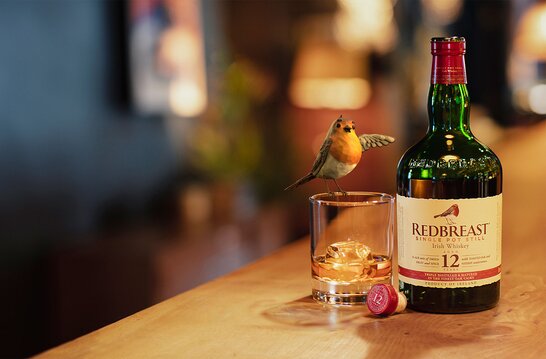 A bottle of Redbreast whiskey next to a glass and an animated robin. 