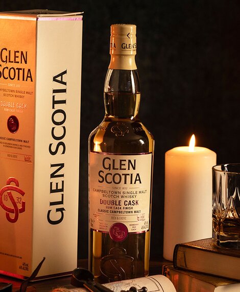 A bottle of Glen Scotia Double Rum Finish whisky next to a stack of books and a candle. 