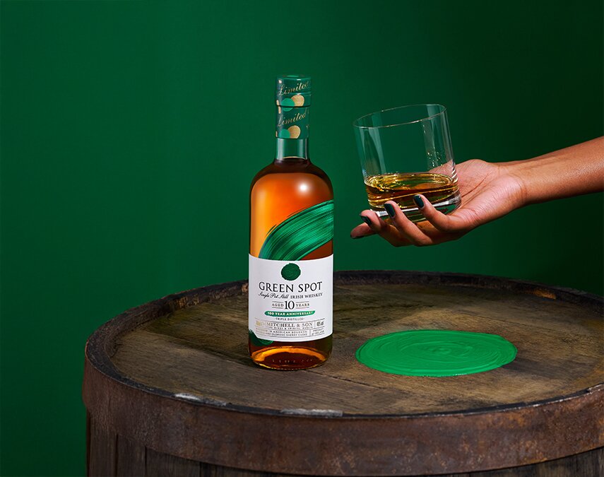 A bottle of Green Spot 10 Year Old 100 Year Anniversary bottle and a woman holding a glass of whiskey.
