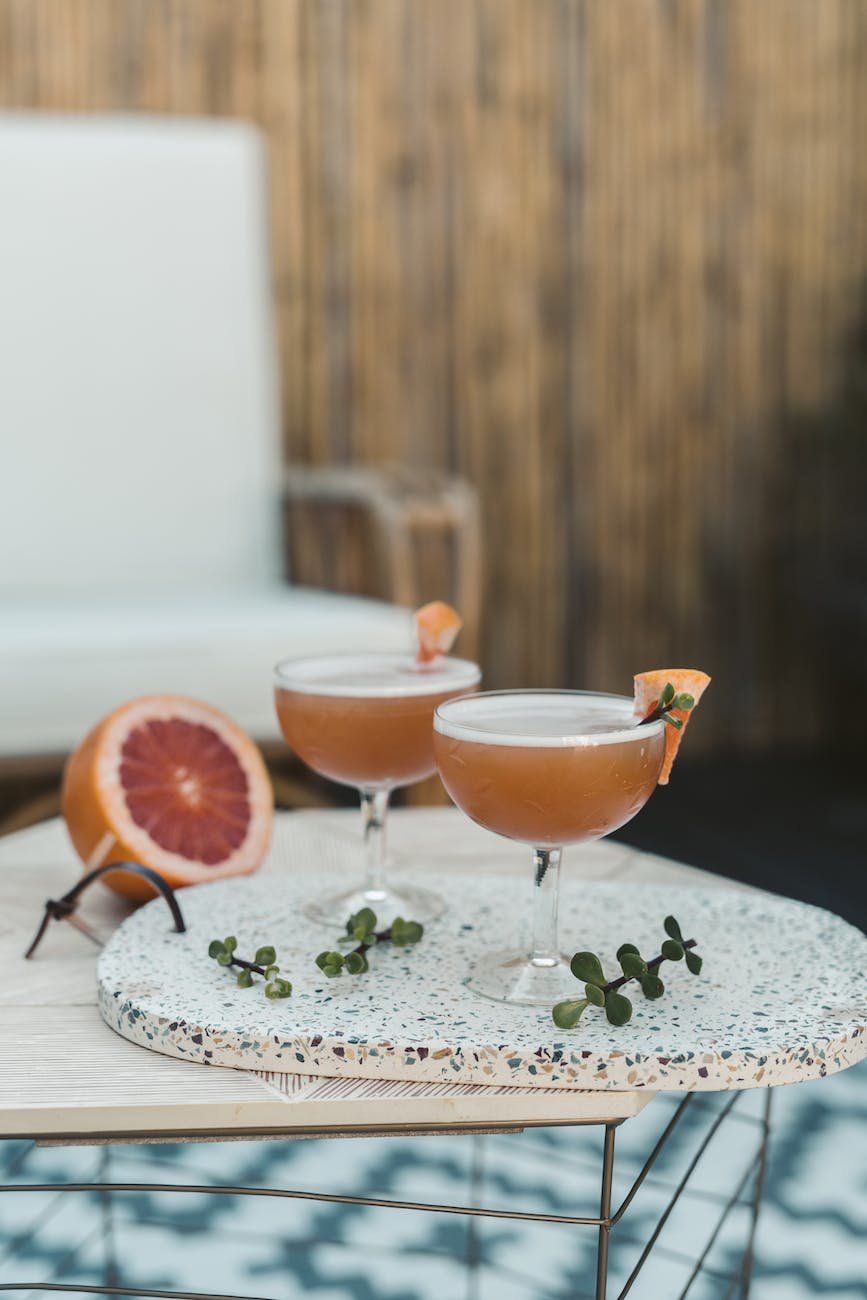 Two coupe glasses filled with a citrussy looking cocktail, perched on a garden table.