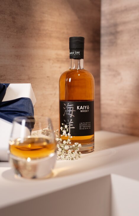 A bottle of Kaiyo whisky against a pink and beige background. 
