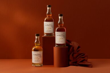 Three bottles of Balvenie whisky on platforms against a rust orange background. 