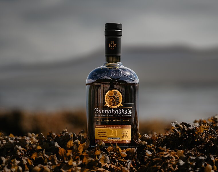 A bottle of Bunnahabhain 21 Year Old Pedro Ximenez Cask Finish amongst seaweed on a beach.