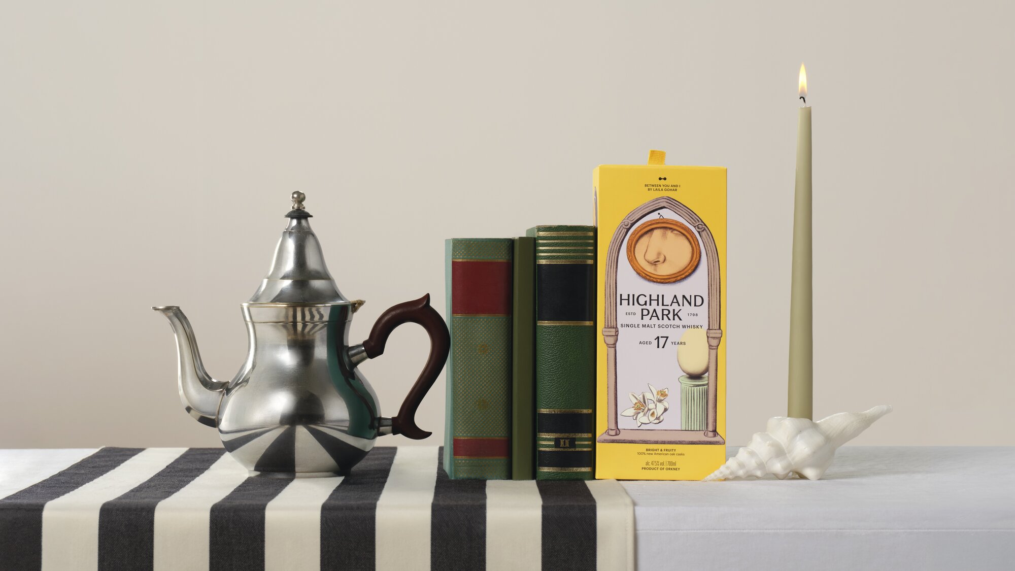 Highland Park Between You & I 2 box next to a teapot, books and a candle. 