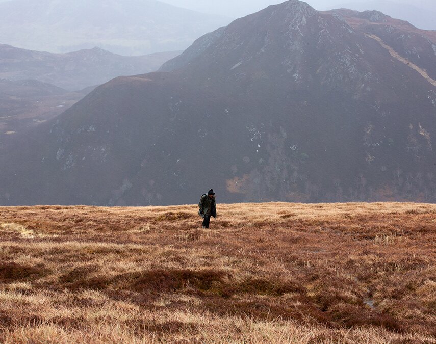 Aldo Kane in a field in front of a mountain.