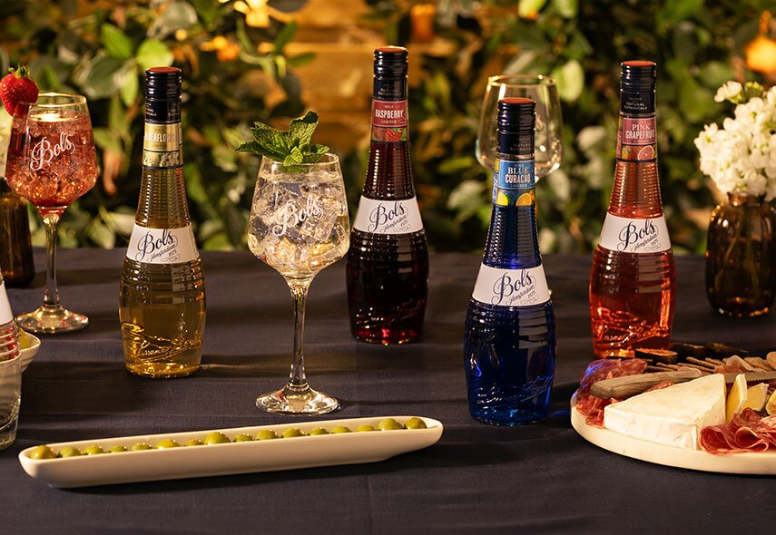 Four bottles of Bols Liqueurs on a table with a charcuterie board. 