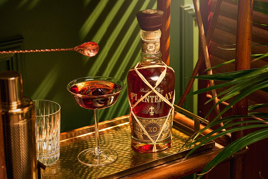 A bottle of XO Planteray Rum next to a Manhattan cocltail.