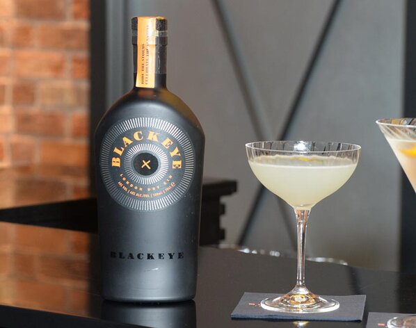 A bottle of Blackeye Gin next to a Lemon Drop cocktail.