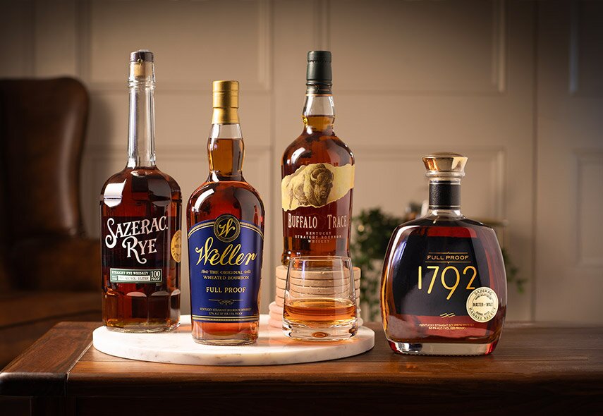 Four bottles of whisky in front of an armchair and paneled wall.
